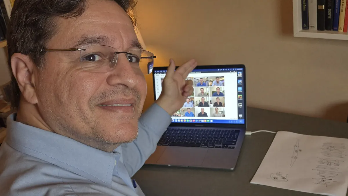 Marcelo conduzindo um encontro ao vivo por vídeo, com o A3 impresso sobre a mesa